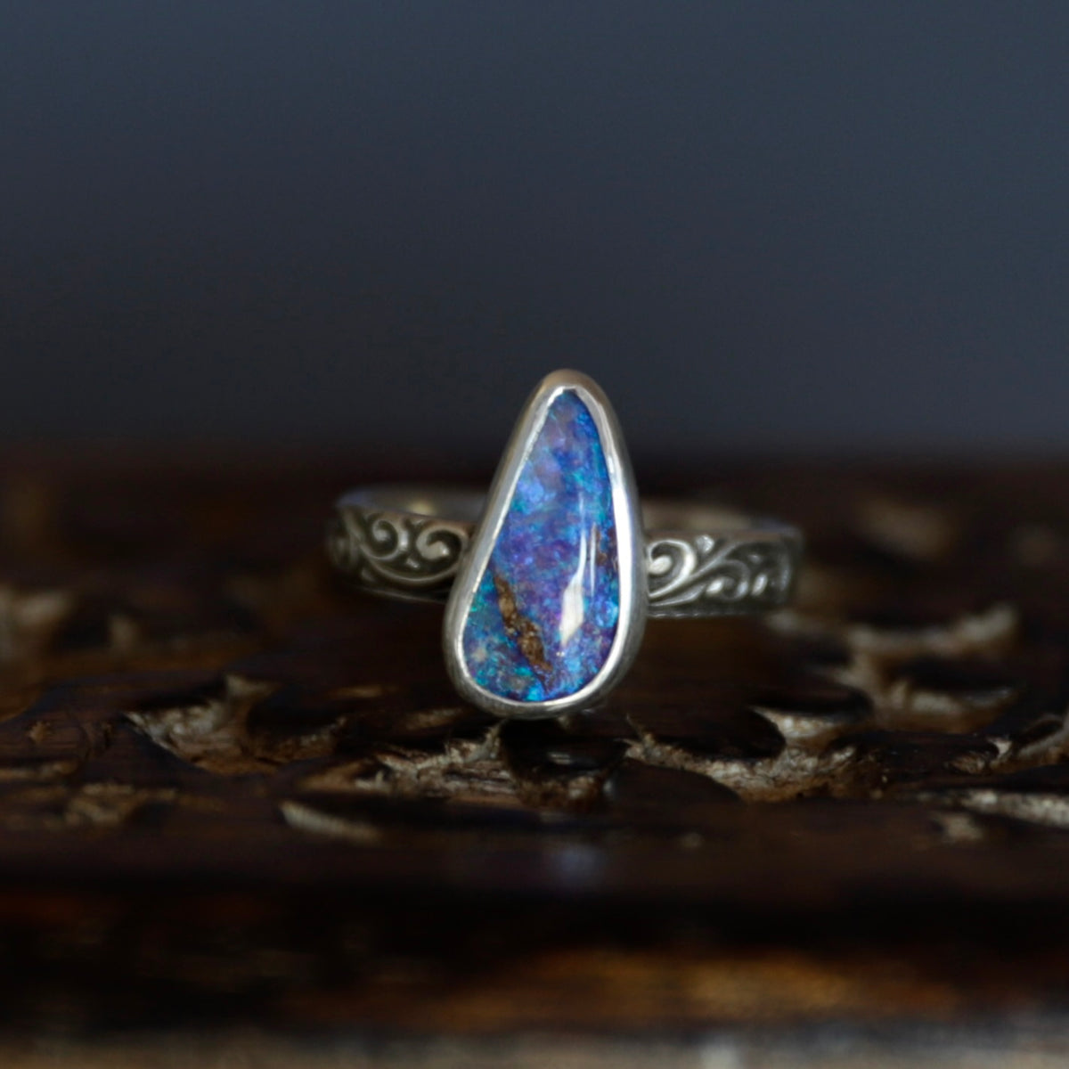 A sterling silver ring with an irregular, teardrop-shaped blue opal gemstone, resting on a dark, carved wooden surface.